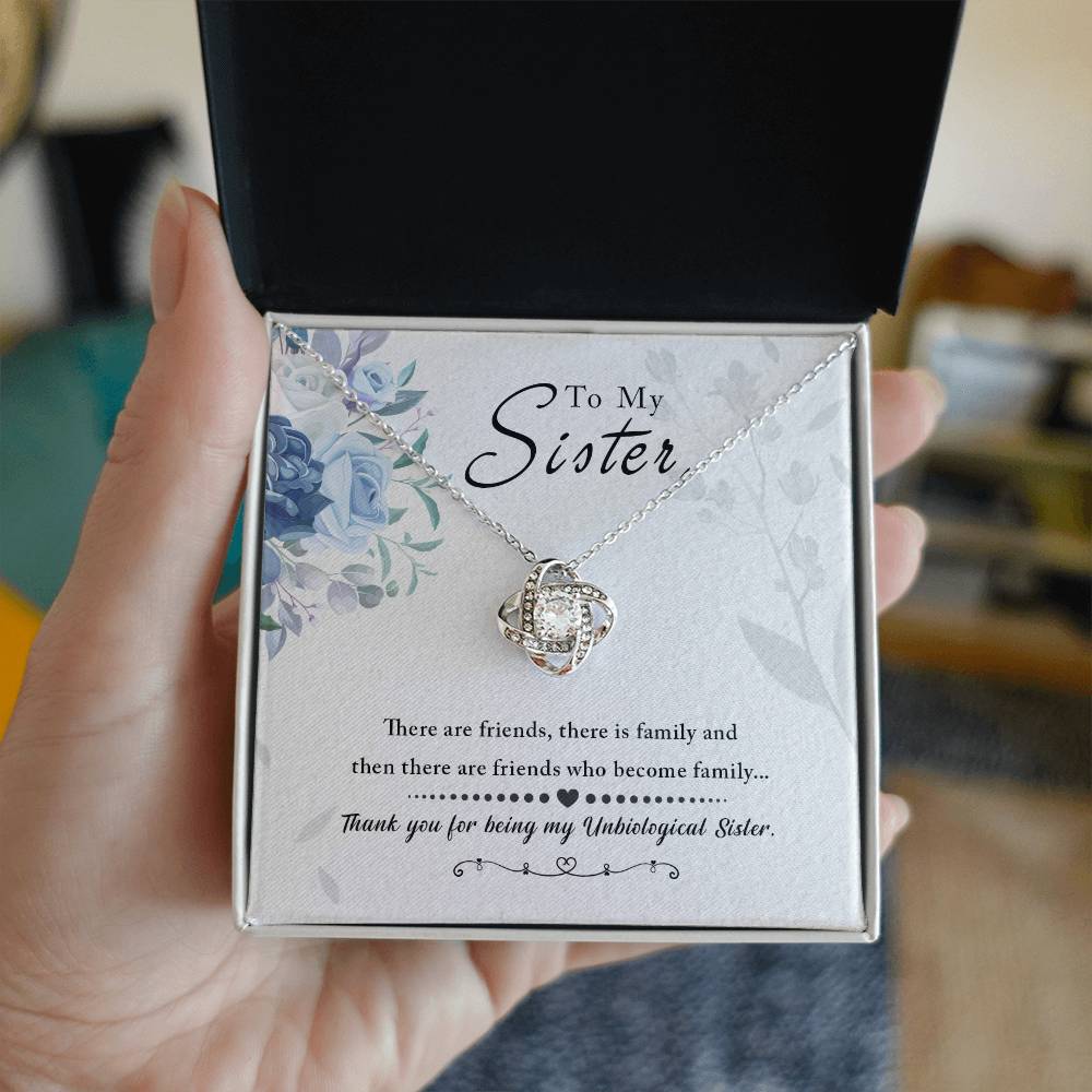 Woman holding a pendant necklace in a box with 'To My Sister' message, featuring a Love Knot design with cubic zirconia crystals.