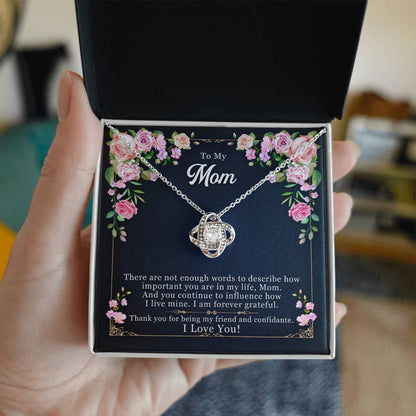 Person holding a Love Knot Necklace in a gift box with the message "To My Mom, Thank You for Being My Friend" and pink floral decorations.