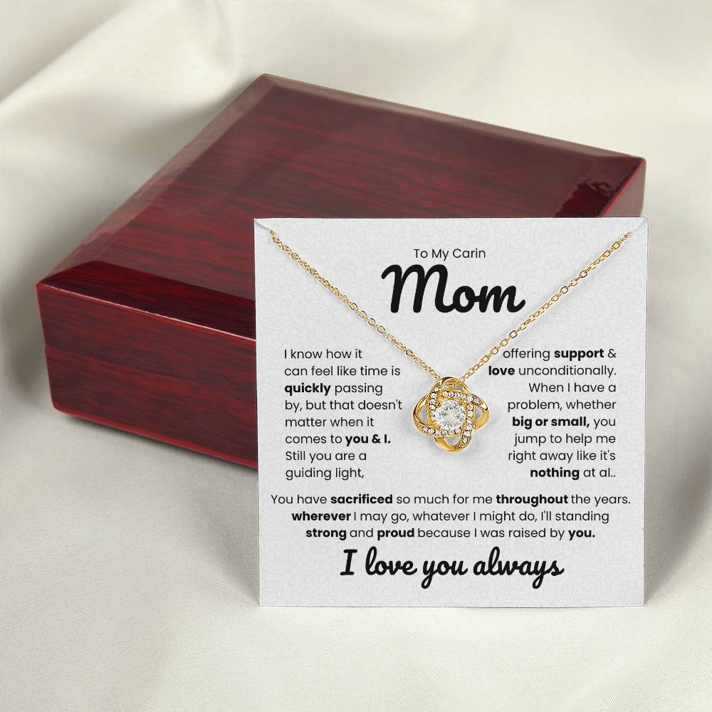 Gold love knot necklace with heartfelt message for mom on display with a wooden jewelry box.