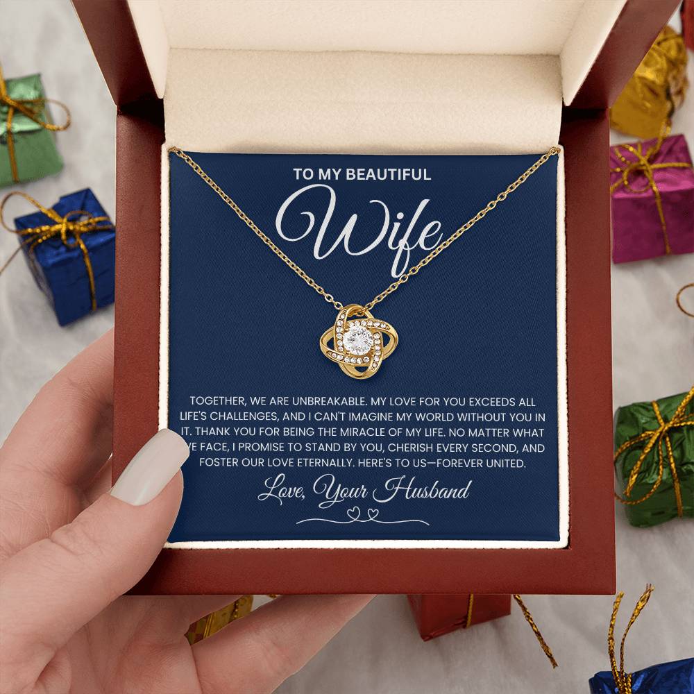 Love Knot Necklace in gift box for wife, featuring sparkling cubic zirconia pendant on gold chain, surrounded by wrapped presents.