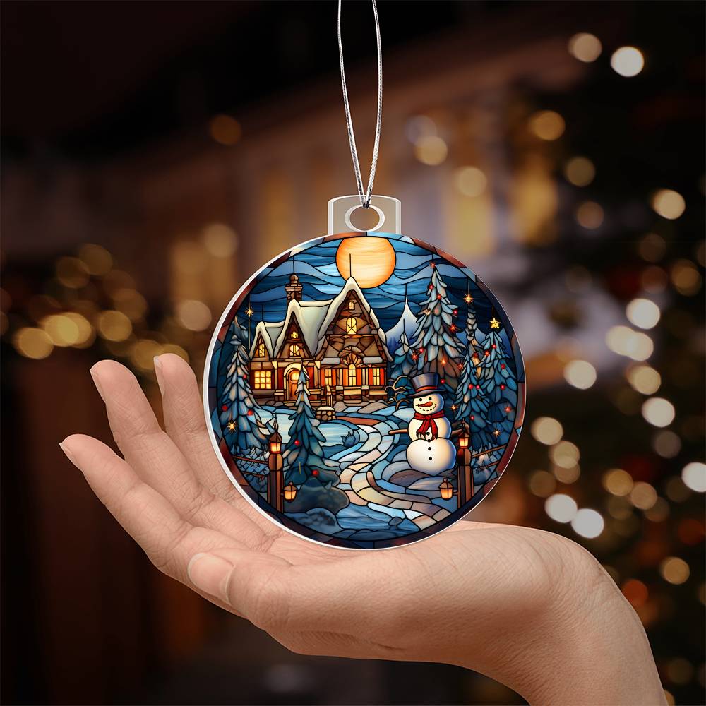 Hand holding Christmas acrylic ornament with snowman and cozy cottage under a full moon, twinkling lights in the background.