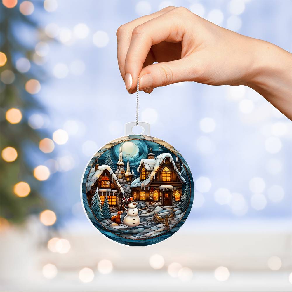 Hand holding Snowy Cottage Christmas Charm acrylic ornament featuring cottages and snowman in a winter scene.